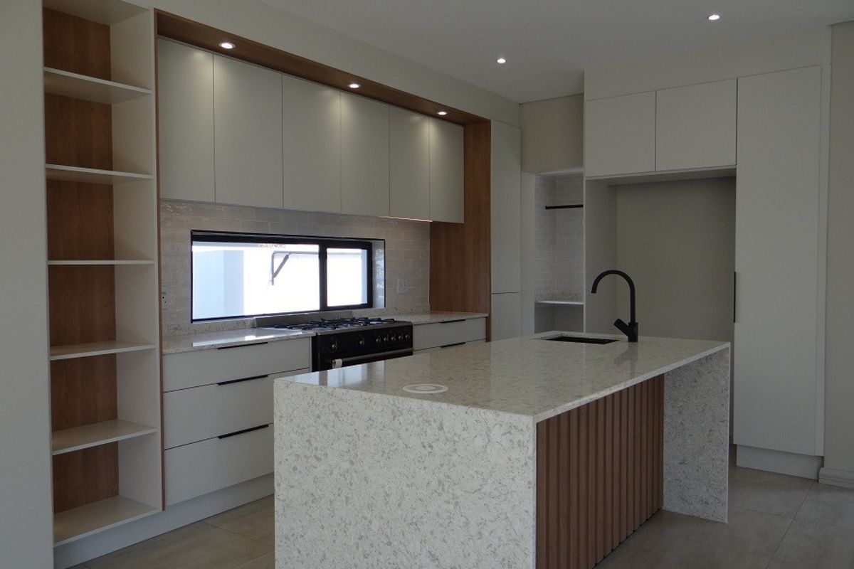 Modern kitchen featuring a large stone-topped island, sleek built-in cabinetry, gas cooktop, and integrated shelving in a clean, contemporary design.