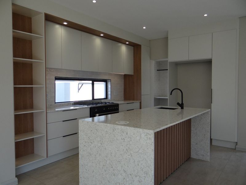 Modern kitchen featuring a large stone-topped island, sleek built-in cabinetry, gas cooktop, and integrated shelving in a clean, contemporary design.
