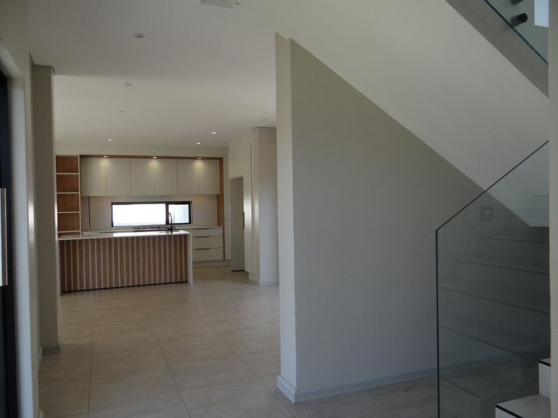 An open-plan living area featuring a modern kitchen with island cabinetry and a staircase with a contemporary glass balustrade.