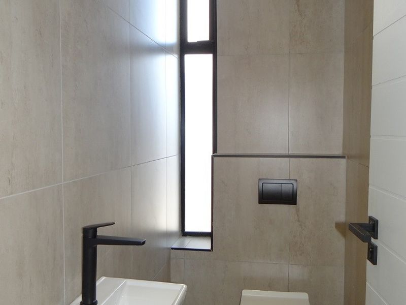 Modern guest bathroom featuring a wall-mounted toilet with concealed cistern, sleek wall-mounted basin with black fixtures, and neutral floor-to-ceiling tiling.