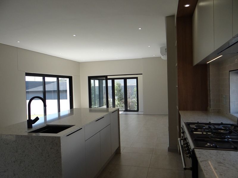 Modern open-plan kitchen and living area featuring a large stone-topped island, gas hob, sleek cabinetry, and expansive sliding doors leading to the outdoors.