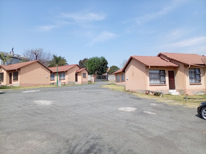 Exterior view of a residential complex featuring multiple single-story units with tiled roofs and paved driveway access.