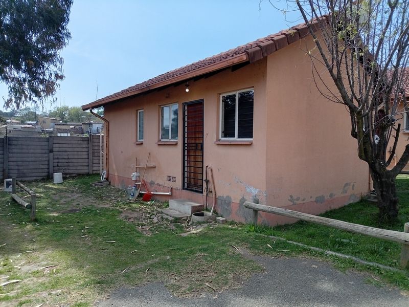 Rear view of a single-story house featuring a tiled roof, security gate, and surrounding garden area with boundary walling.