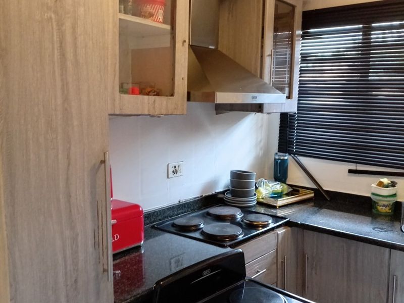 Compact kitchen featuring granite countertops, built-in cabinetry, an extractor fan, and an electric stove with a window providing natural light.