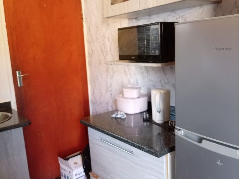 A compact kitchen area featuring built-in cabinetry, granite countertops, and tiled flooring, currently showing signs of wear on the cabinet finishes.