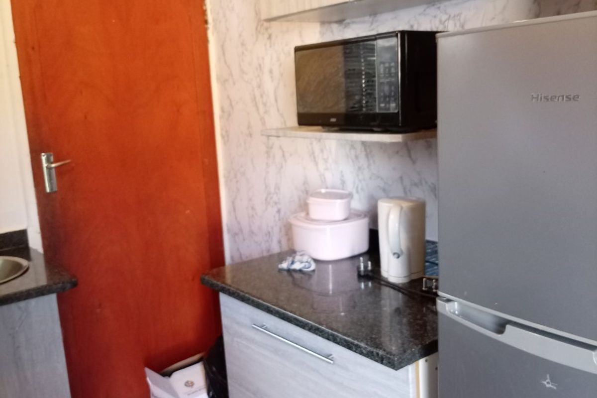 A compact kitchen area featuring built-in cabinetry, granite countertops, and tiled flooring, currently showing signs of wear on the cabinet finishes.