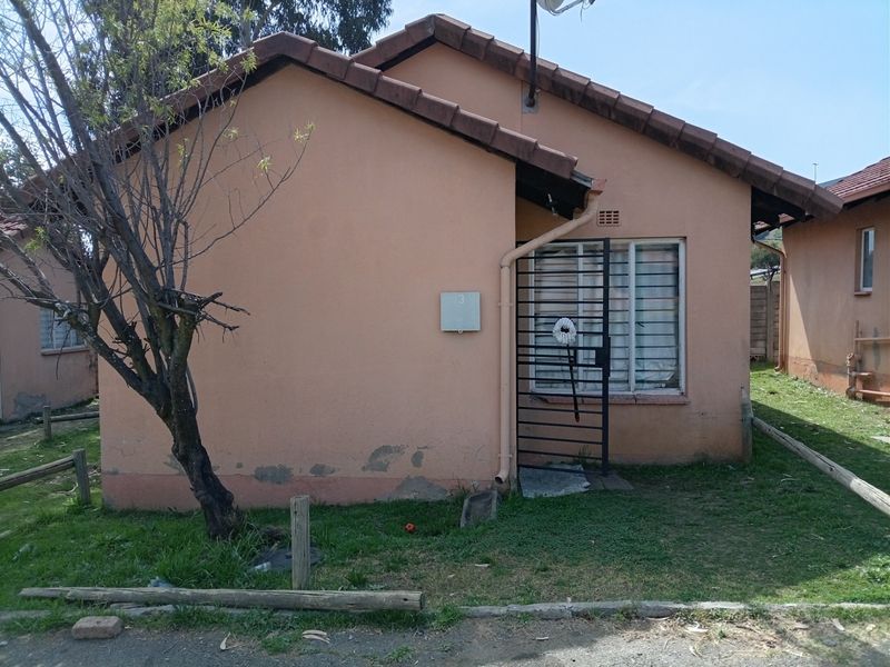 Front elevation of a single-story house featuring a tiled roof, security gate, and plastered exterior walls showing signs of wear.