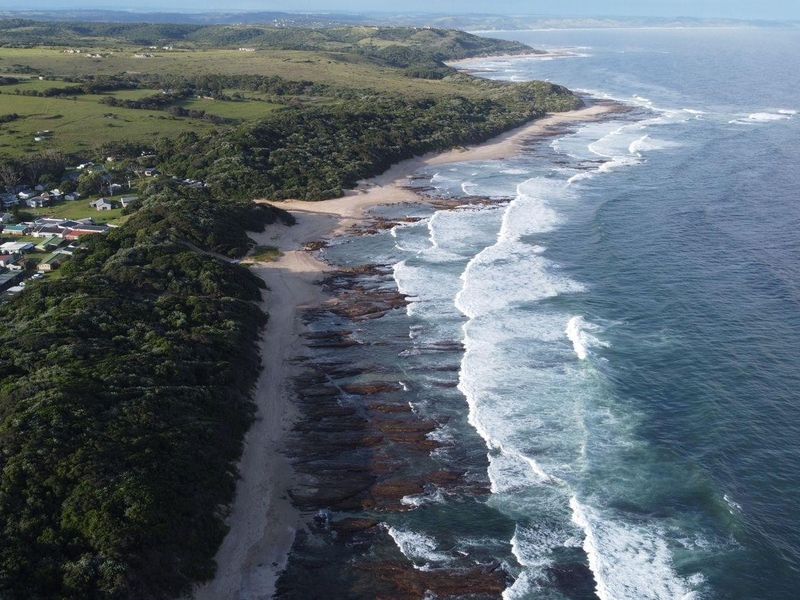 An aerial view of the coastal landscape, showcasing the beach, ocean, and surrounding natural terrain near the residential area.