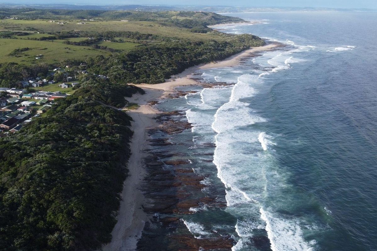 An aerial view of the coastal landscape, showcasing the beach, ocean, and surrounding natural terrain near the residential area.