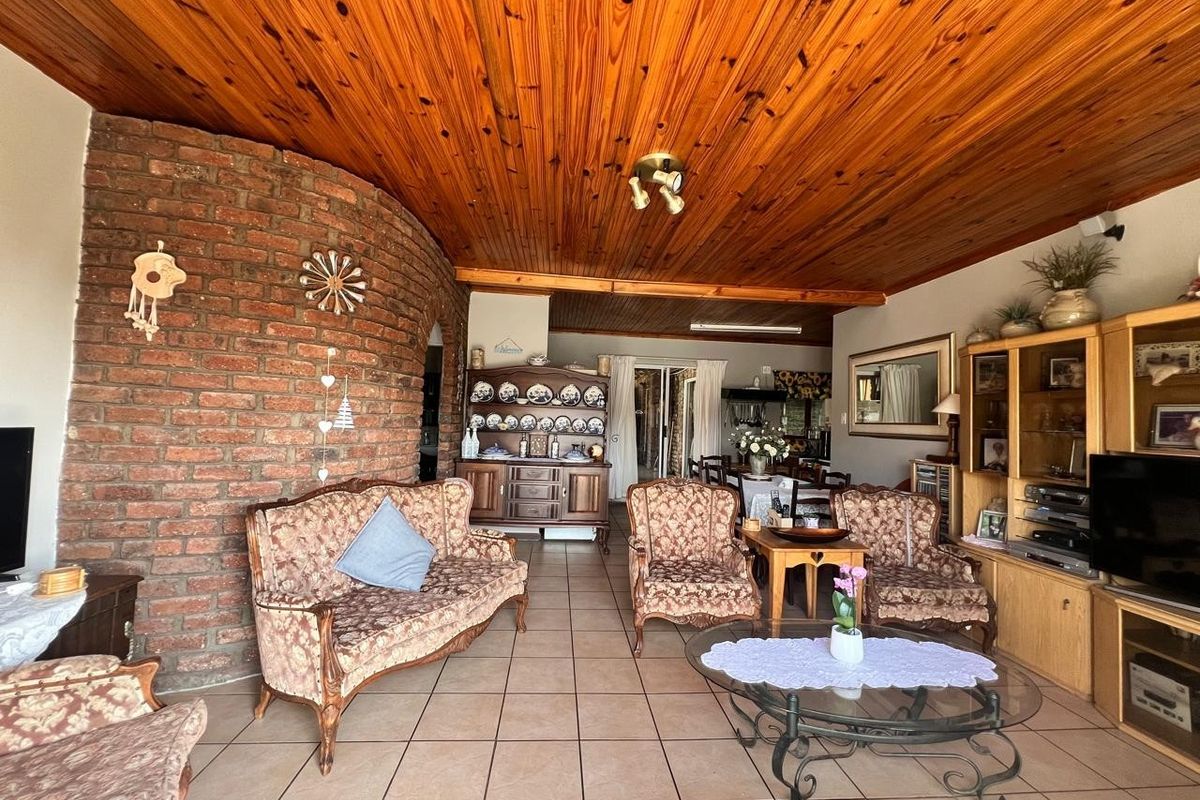 Spacious living area featuring a distinctive exposed brick feature wall, warm timber tongue and groove ceiling, and neutral ceramic floor tiles.