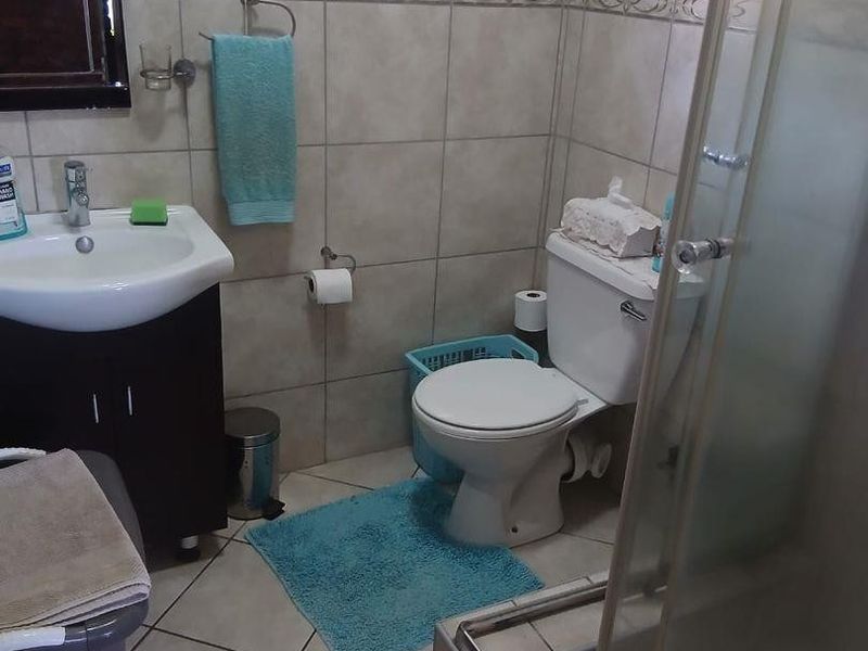 A functional bathroom featuring a vanity cabinet, toilet, and a glass-enclosed shower with neutral ceramic wall and floor tiling.