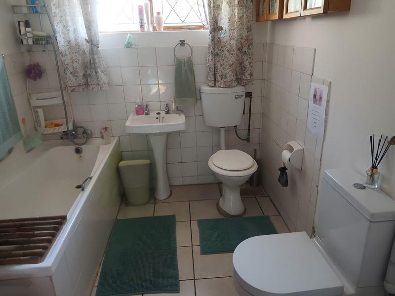 A dated bathroom featuring a pedestal basin, toilet, and bathtub with wall and floor tiling, requiring modernization to improve its overall condition and appeal.