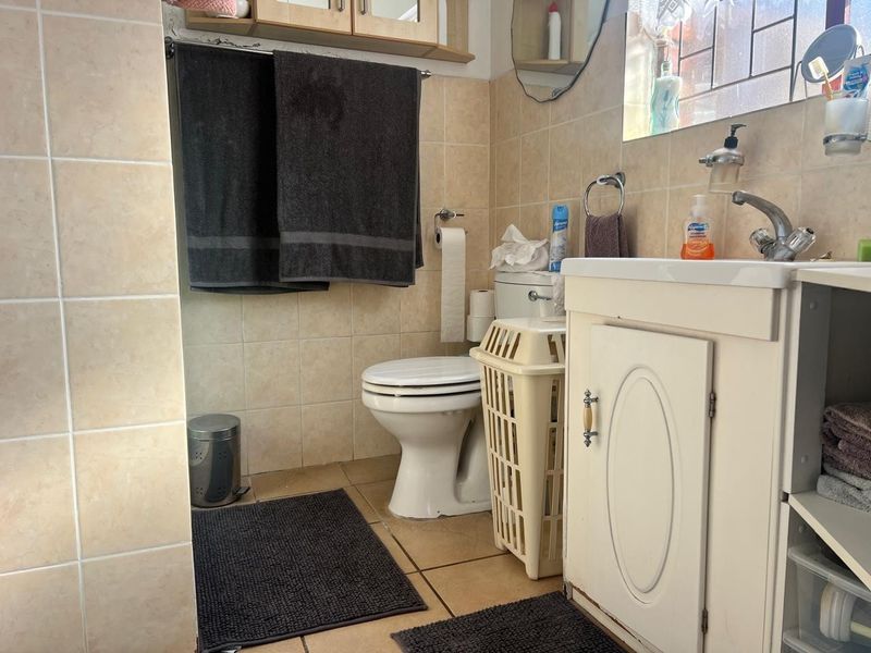 A functional bathroom featuring a vanity cabinet, ceramic basin, and wall-to-floor tiling, offering a practical layout with potential for cosmetic updates.