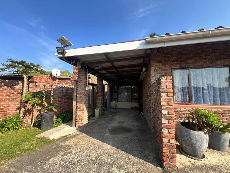 A rear exterior view featuring a brick facade, a covered carport area, and a concrete driveway with integrated solar security lighting.