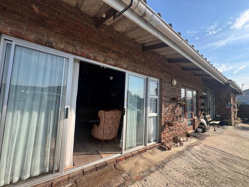 Rear exterior view featuring exposed brick walls, sliding glass doors leading to the interior, and a concrete patio area with exposed timber rafters.