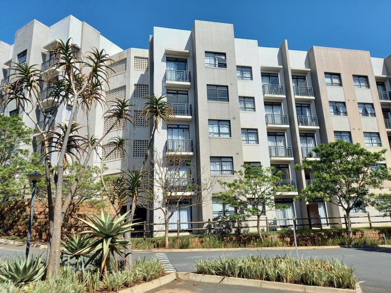 A modern multi-story apartment complex featuring a clean concrete facade, multiple private balconies with sliding glass doors, and decorative architectural breeze block detailing.