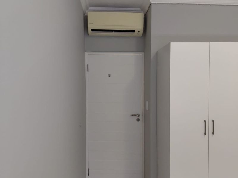 A bedroom interior featuring neutral grey walls, tiled flooring, crown molding, a built-in wardrobe, and a wall-mounted air conditioning unit.