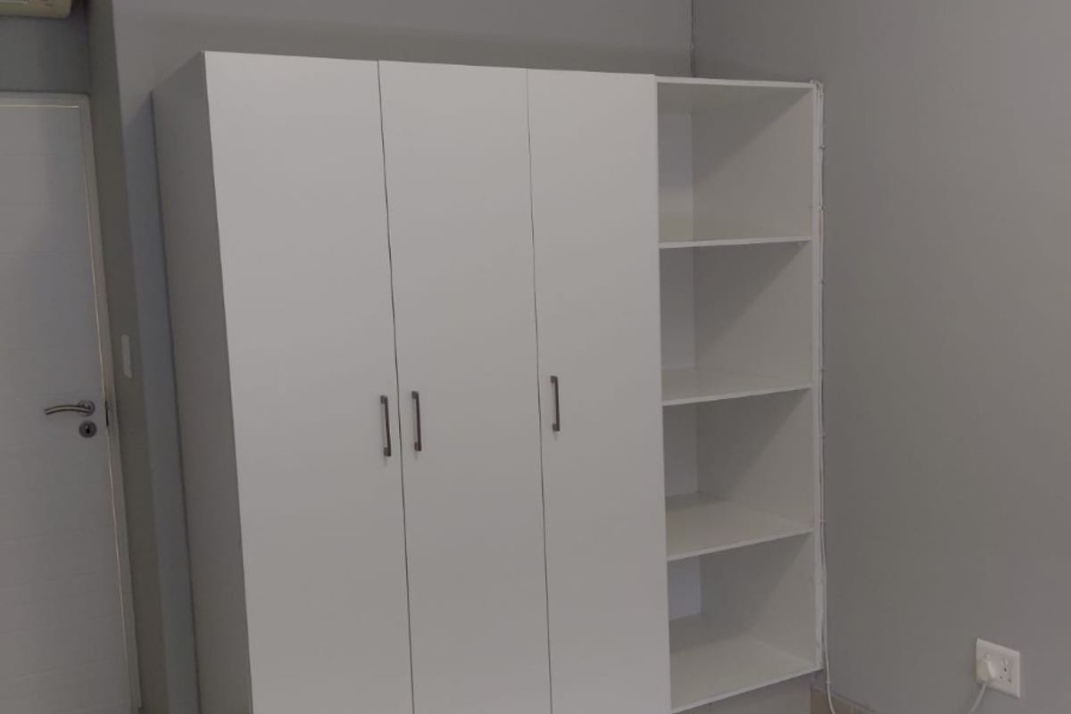 A clean bedroom featuring a modern white built-in wardrobe with integrated open shelving, tiled floors, and a wall-mounted air conditioning unit.