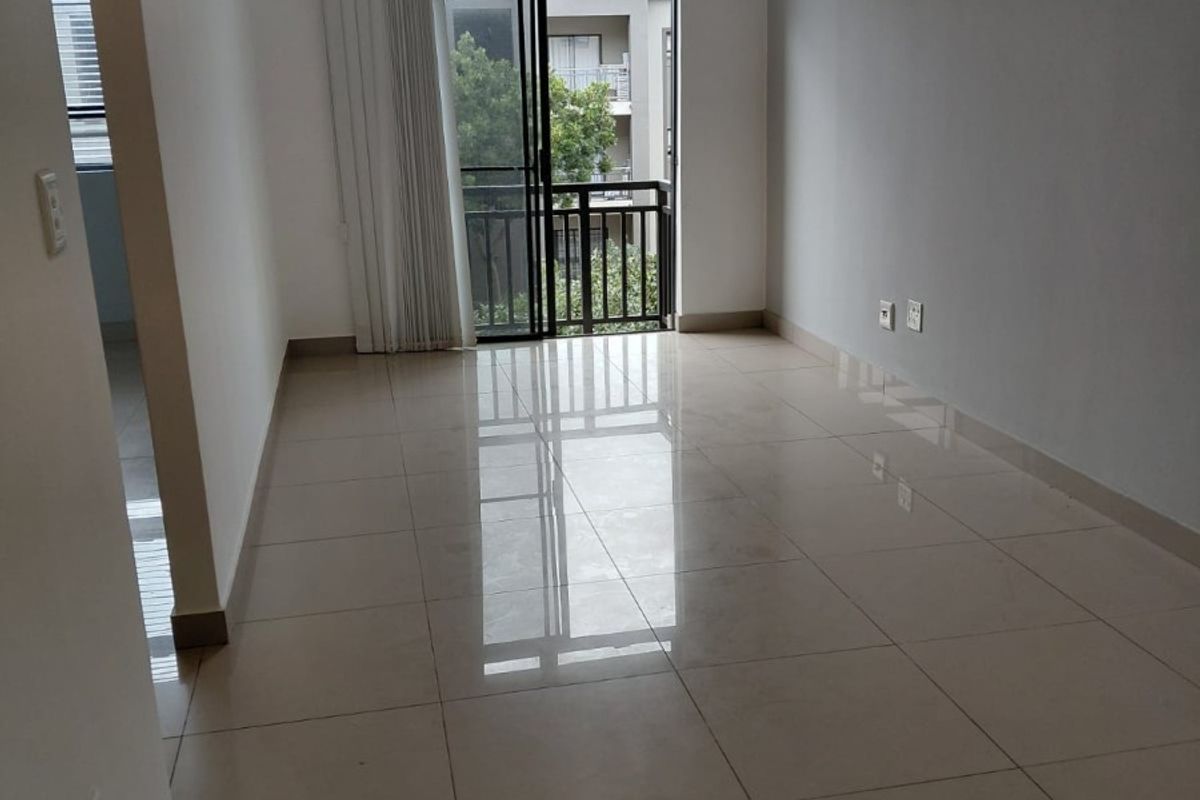 An empty, well-maintained living area featuring neutral tiled flooring, clean walls, and a sliding glass door providing access to a private balcony.