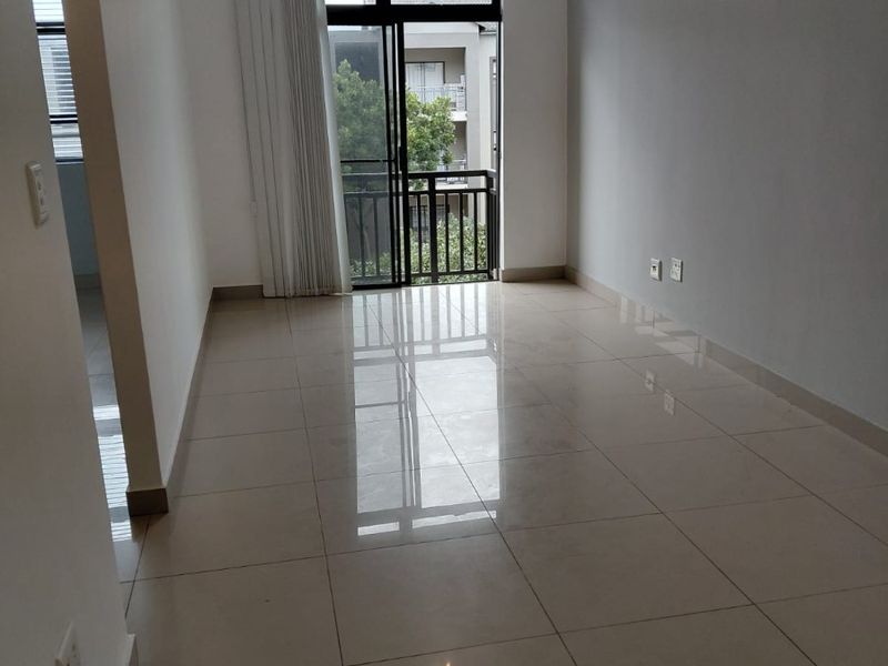 An empty, well-maintained living area featuring neutral tiled flooring, clean walls, and a sliding glass door providing access to a private balcony.