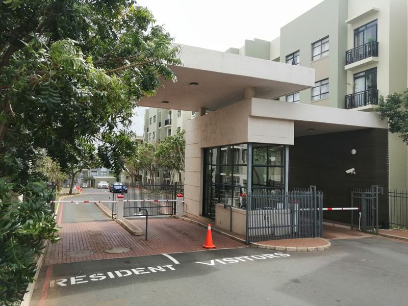 The apartment complex features a secure gated entrance with a dedicated security guardhouse, boom gate access control, and paved driveway for residents and visitors.