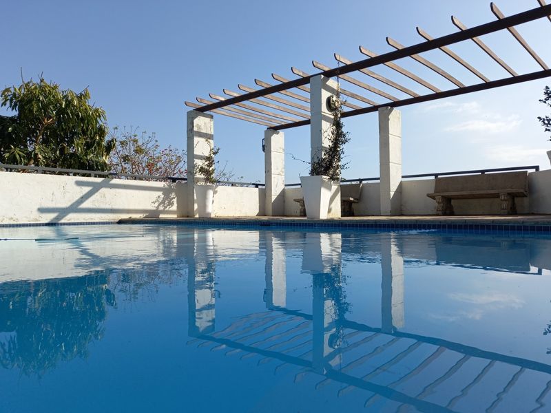 Outdoor pool area featuring a wooden pergola structure, concrete pillars, and a perimeter wall, providing a functional space for relaxation.