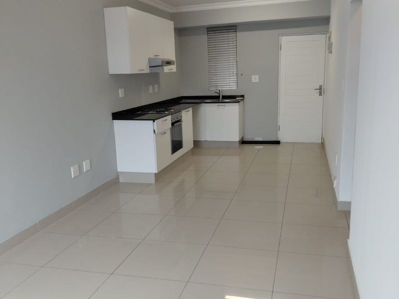 A clean, modern kitchen featuring white cabinetry, black granite countertops, built-in oven and hob, and neutral tiled flooring in an open-plan layout.