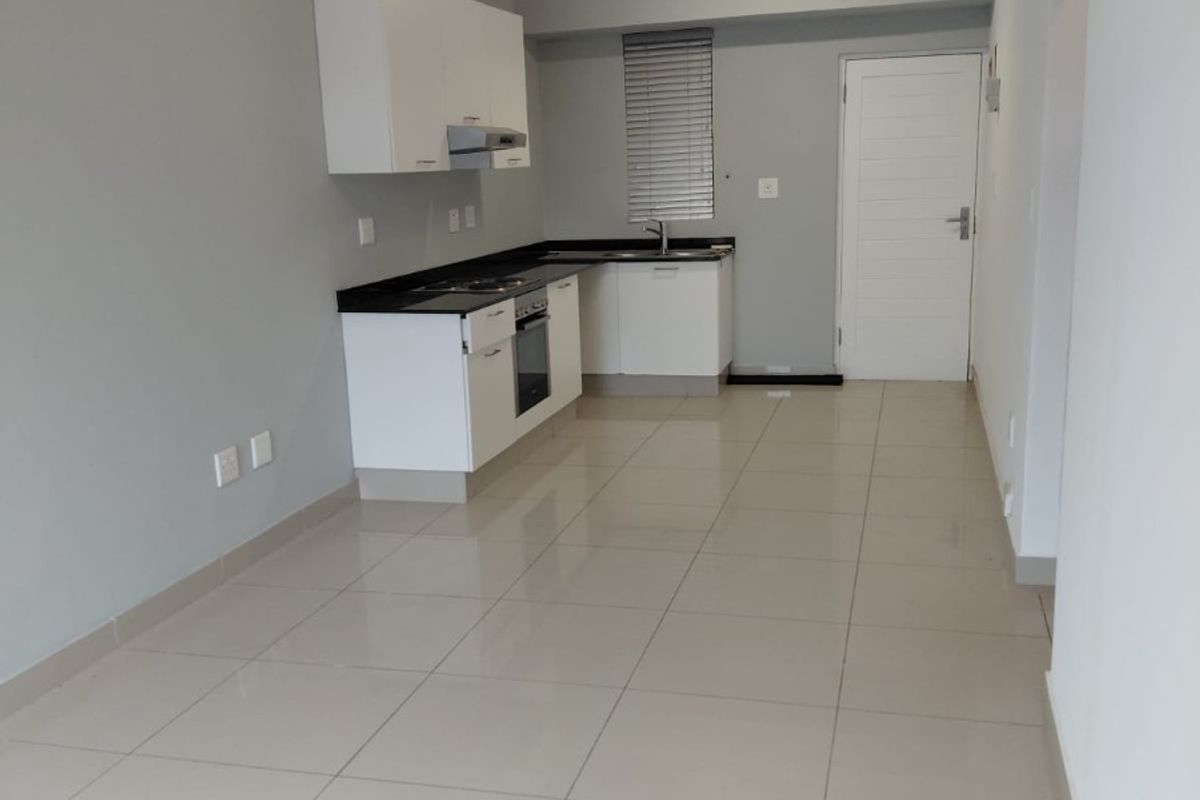 A clean, modern kitchen featuring white cabinetry, black granite countertops, built-in oven and hob, and neutral tiled flooring in an open-plan layout.