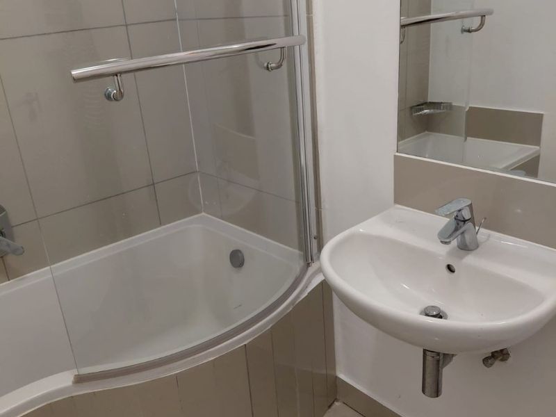 A clean, functional bathroom featuring a curved shower bath with a glass screen, wall-mounted basin, and neutral tiling.