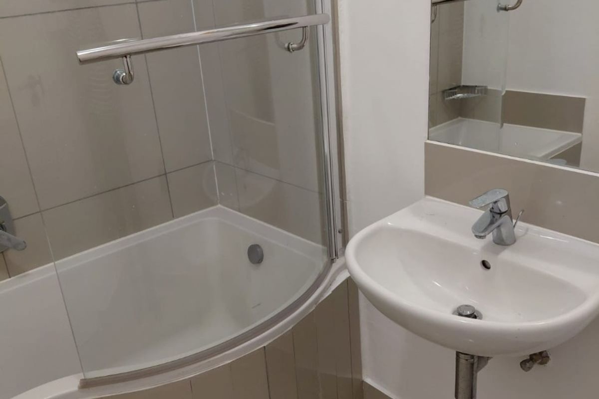 A clean, functional bathroom featuring a curved shower bath with a glass screen, wall-mounted basin, and neutral tiling.