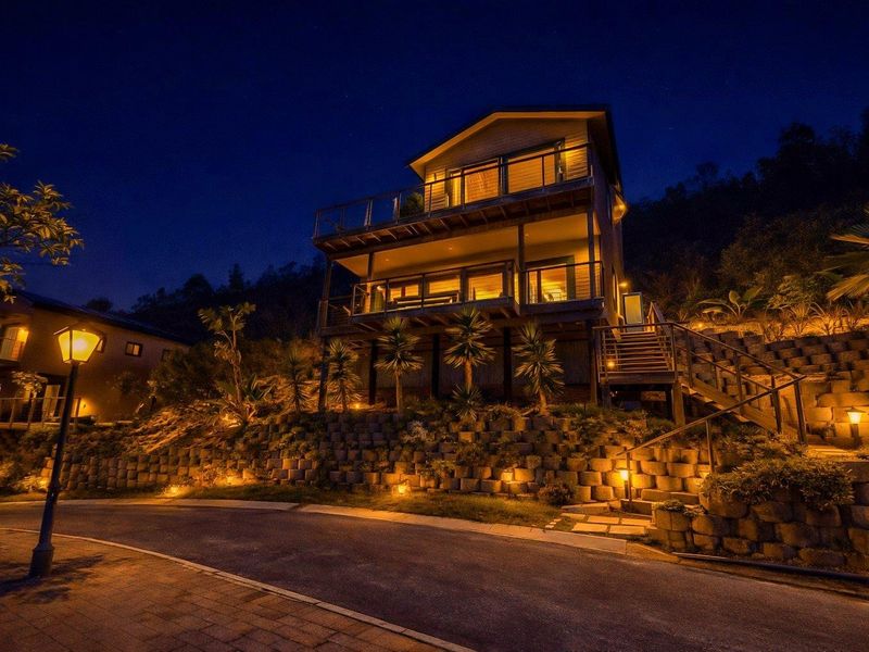 A striking multi-level residential property at night, featuring tiered retaining walls, illuminated balconies, and a well-maintained exterior staircase leading to the entrance.