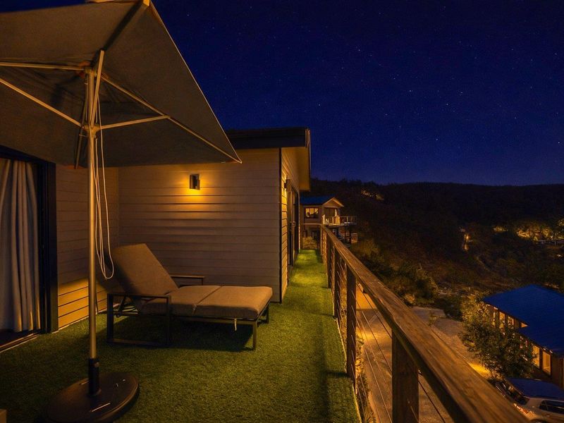 A well-lit balcony at night featuring artificial turf flooring, timber railings, and scenic views of the surrounding landscape.