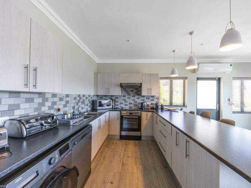 Modern kitchen featuring light wood cabinetry, dark laminate countertops, tiled backsplash, integrated appliances, and a spacious breakfast bar with pendant lighting.