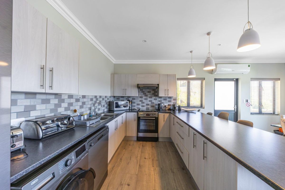 Modern kitchen featuring light wood cabinetry, dark laminate countertops, tiled backsplash, integrated appliances, and a spacious breakfast bar with pendant lighting.