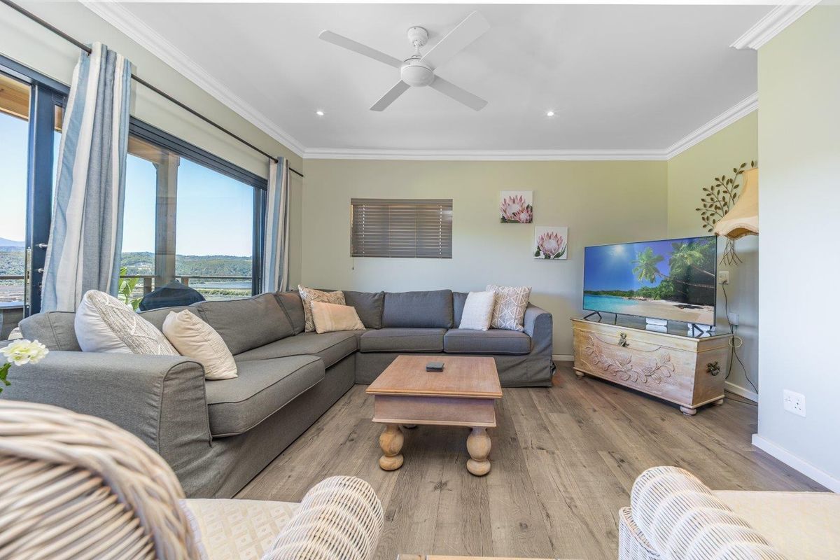 A bright and well-maintained living room featuring laminate flooring, recessed lighting, a ceiling fan, and large sliding glass doors with scenic views.