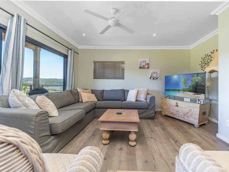A bright and well-maintained living room featuring laminate flooring, recessed lighting, a ceiling fan, and large sliding glass doors with scenic views.