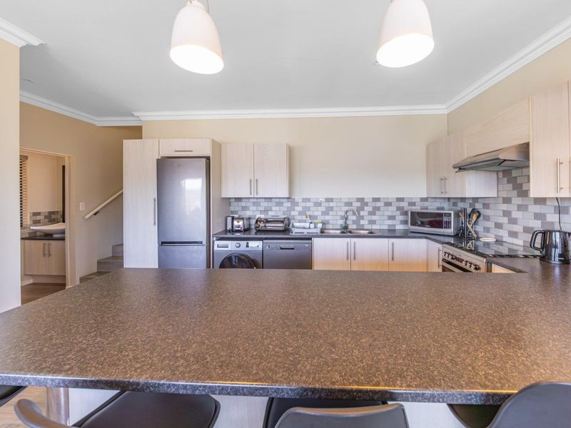 Modern kitchen featuring light wood-tone cabinetry, stone-look countertops, a subway tile backsplash, and integrated stainless steel appliances with a breakfast bar.
