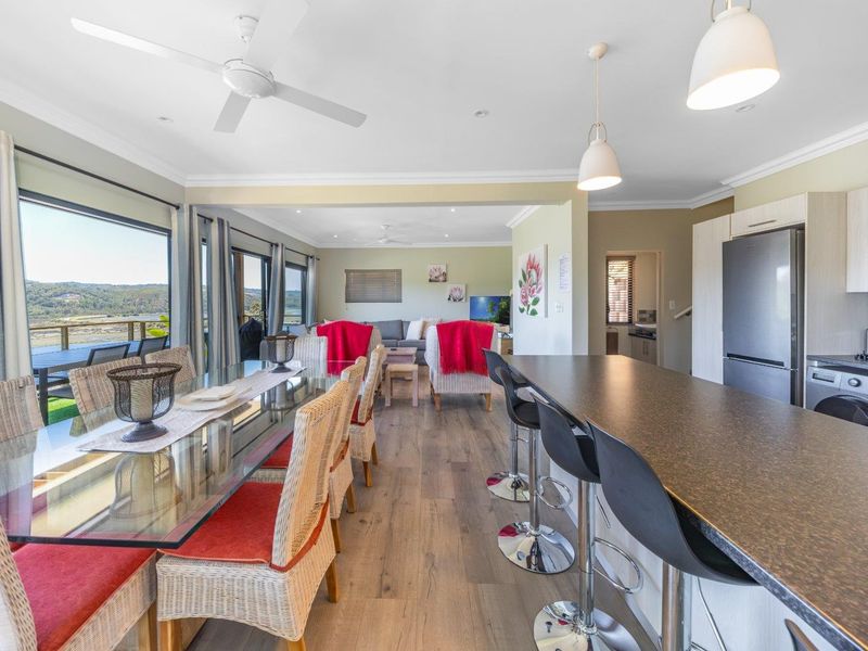 Spacious open-plan living, dining, and kitchen area featuring modern laminate flooring, contemporary lighting, and large sliding doors leading to an outdoor deck with views.