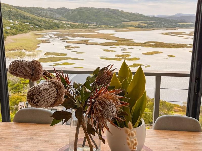 A scenic view of a river estuary and surrounding hills captured through a large sliding glass door with a balcony railing.