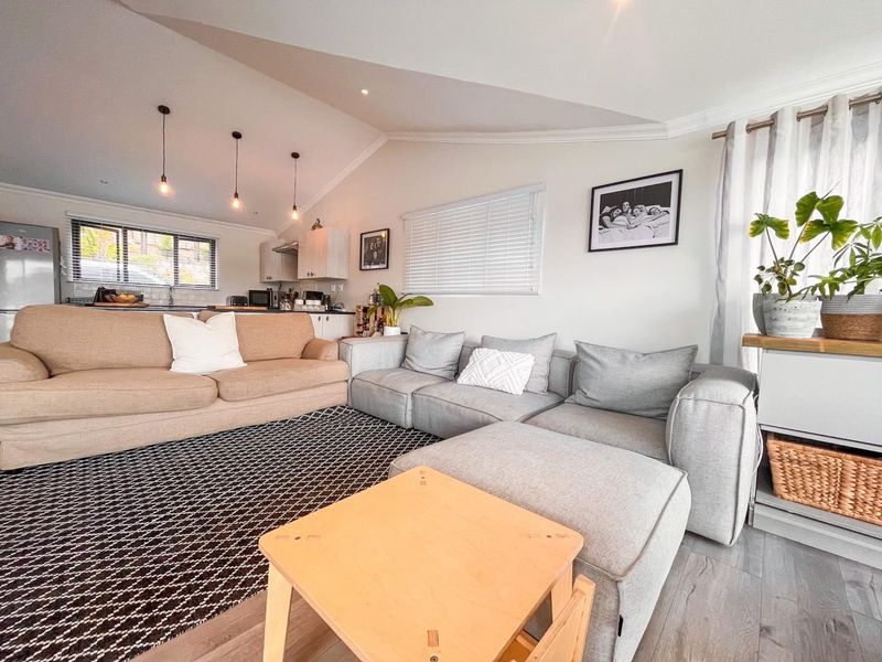 An open-plan living area featuring a vaulted ceiling, laminate flooring, and a connected kitchen space with modern cabinetry and pendant lighting.