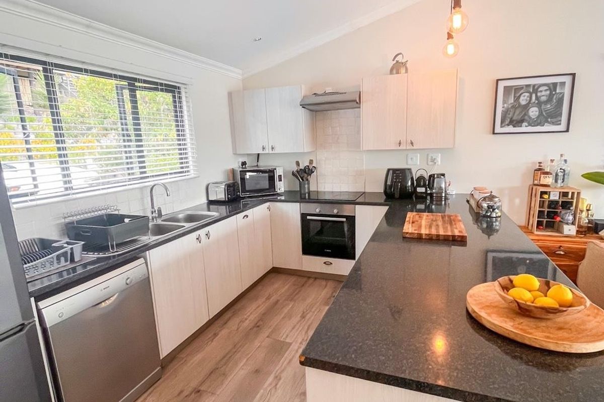 Modern kitchen featuring light wood cabinetry, dark granite countertops, a spacious island, and integrated stainless steel appliances with contemporary pendant lighting.