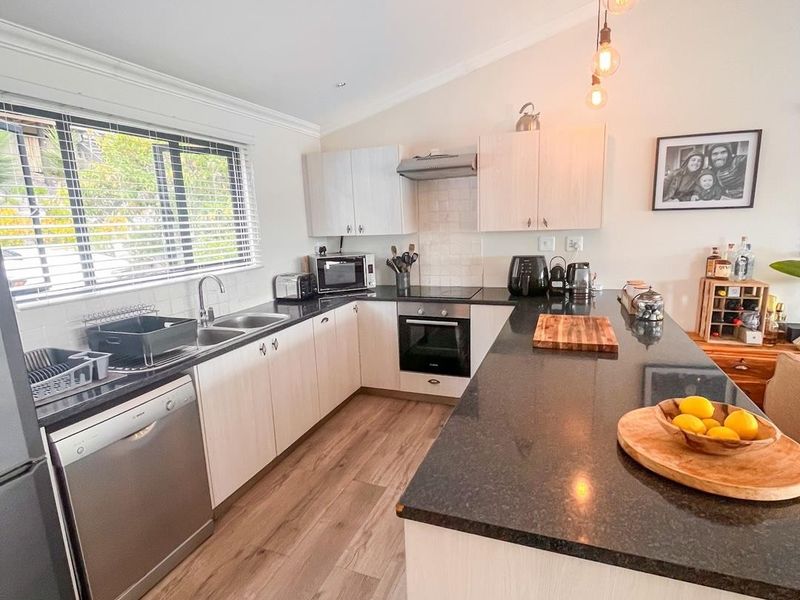 Modern kitchen featuring light wood cabinetry, dark granite countertops, a spacious island, and integrated stainless steel appliances with contemporary pendant lighting.