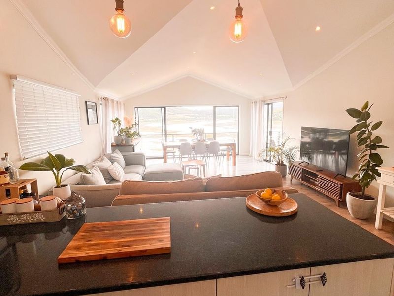 Spacious open-plan living area featuring a modern kitchen island with granite countertops, vaulted ceilings, and large sliding doors leading to an outdoor view.