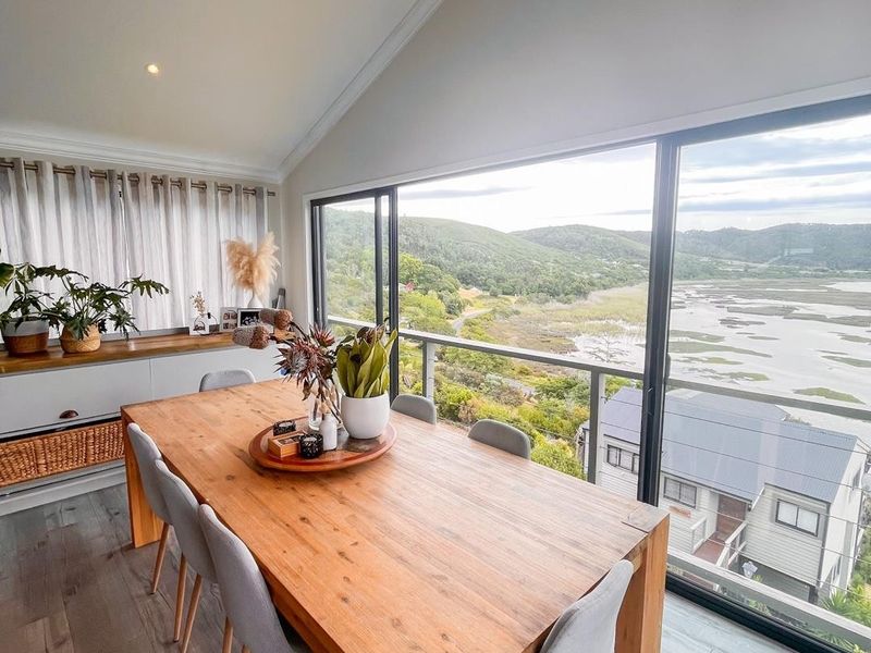 Bright dining area featuring a vaulted ceiling, modern laminate flooring, and expansive sliding glass doors offering panoramic views of the surrounding landscape.