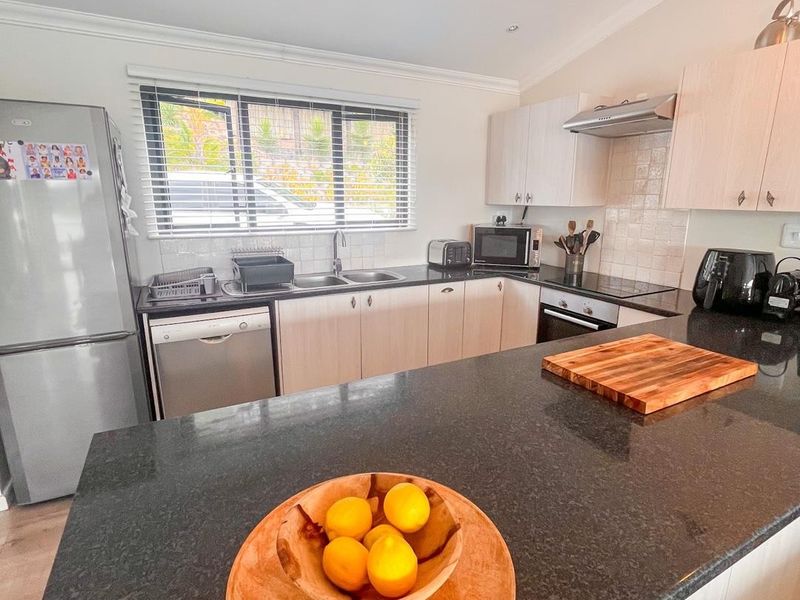Modern kitchen featuring granite countertops, light wood cabinetry, built-in oven, extractor fan, and a functional layout with integrated dishwasher.