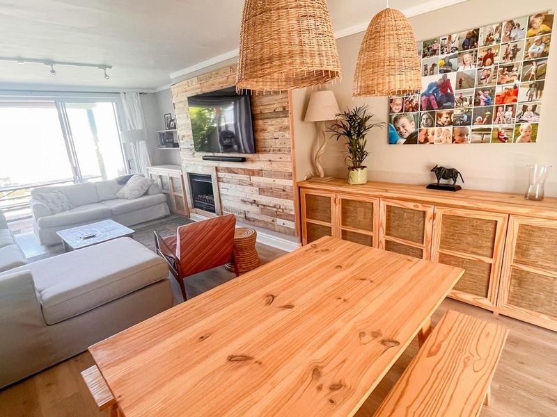 Spacious open-plan living and dining area featuring timber wall cladding, a fireplace, laminate flooring, and large sliding doors leading to the exterior.