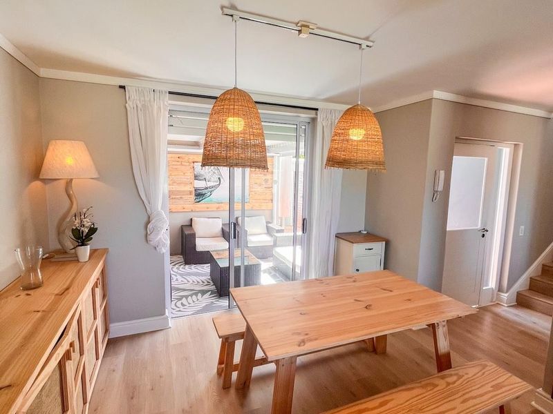 A bright dining area featuring light wood laminate flooring, coving, and a sliding glass door providing direct access to an outdoor patio space.