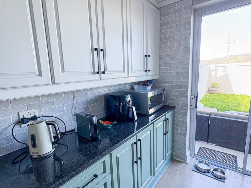 A well-maintained scullery featuring shaker-style cabinetry, granite countertops, subway tile backsplash, and direct access to the rear patio.
