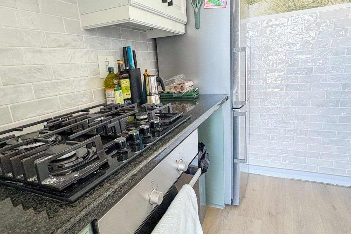 A functional kitchen featuring a gas cooktop, built-in oven, extractor fan, granite countertops, and subway tile backsplash with light-toned laminate flooring.
