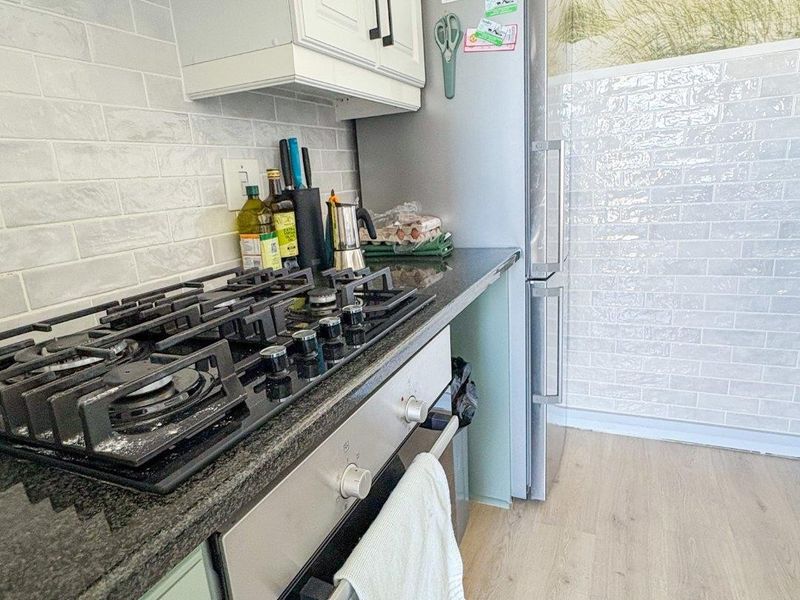 A functional kitchen featuring a gas cooktop, built-in oven, extractor fan, granite countertops, and subway tile backsplash with light-toned laminate flooring.